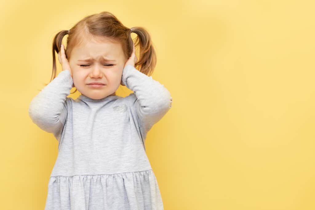 Why do kids hit themselves - Girl covering her ears to prevent sensory overload.