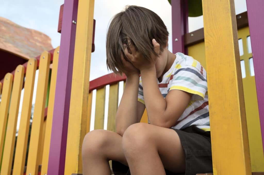 Sad boy in the park covering his face.