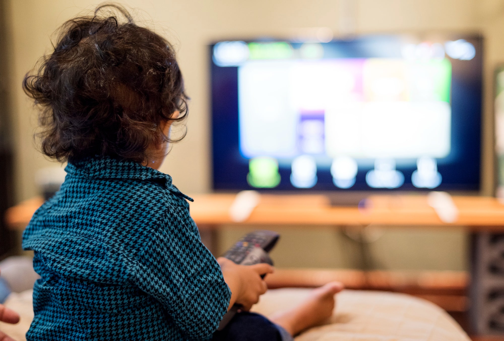 Young boy sitting alone in front of a television captivated by the content on the screen.