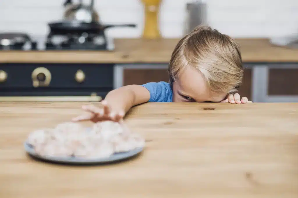 Little boy reaching to grab a cookie from the kitchen table