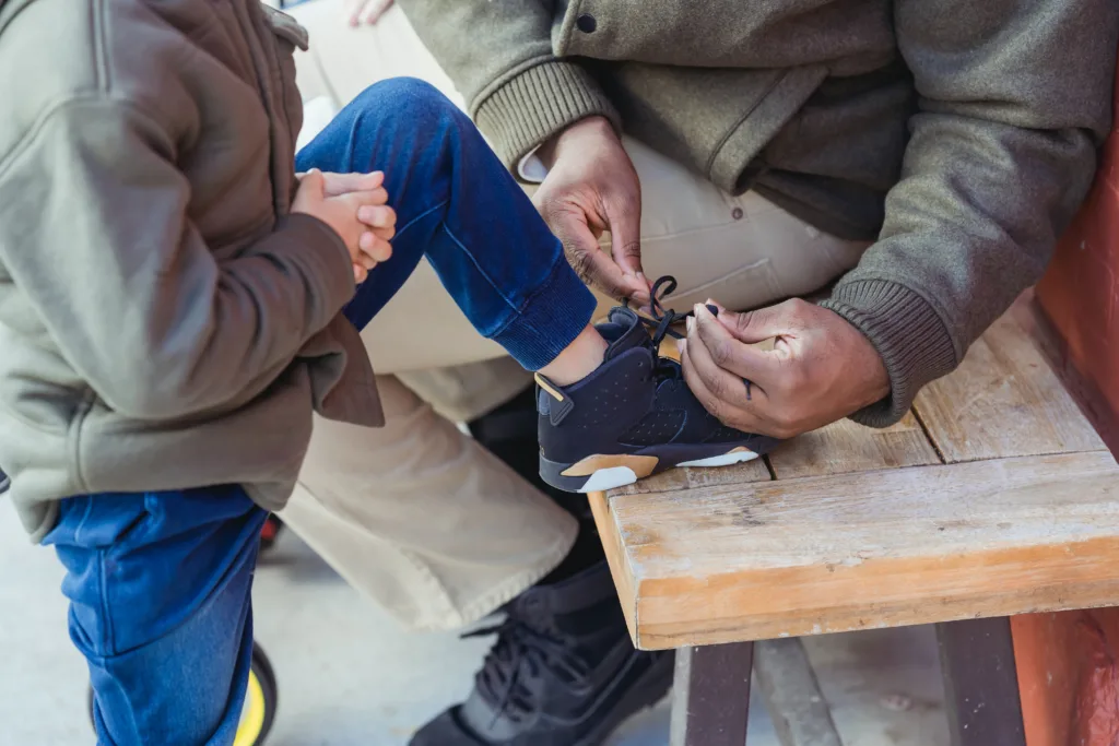 Father sitting on a bench tying his son’s shoelaces 