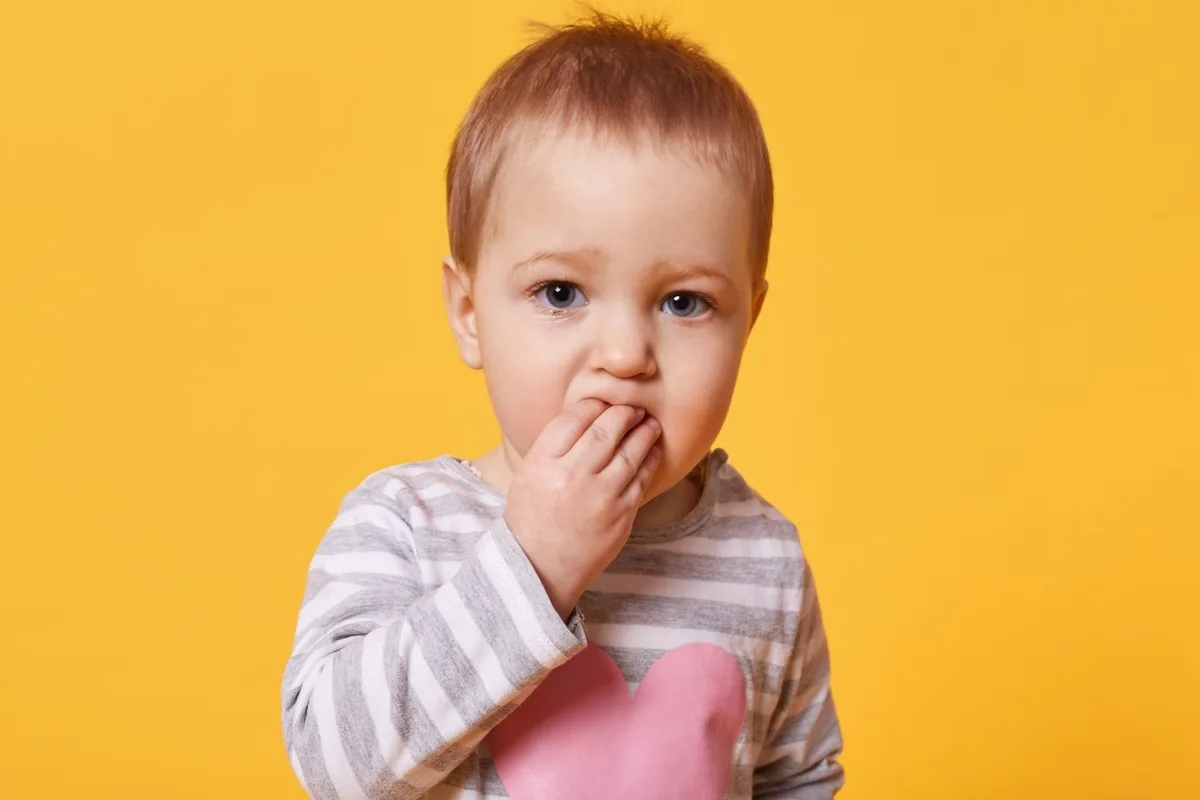 A close up picture of a toddler biting his hand