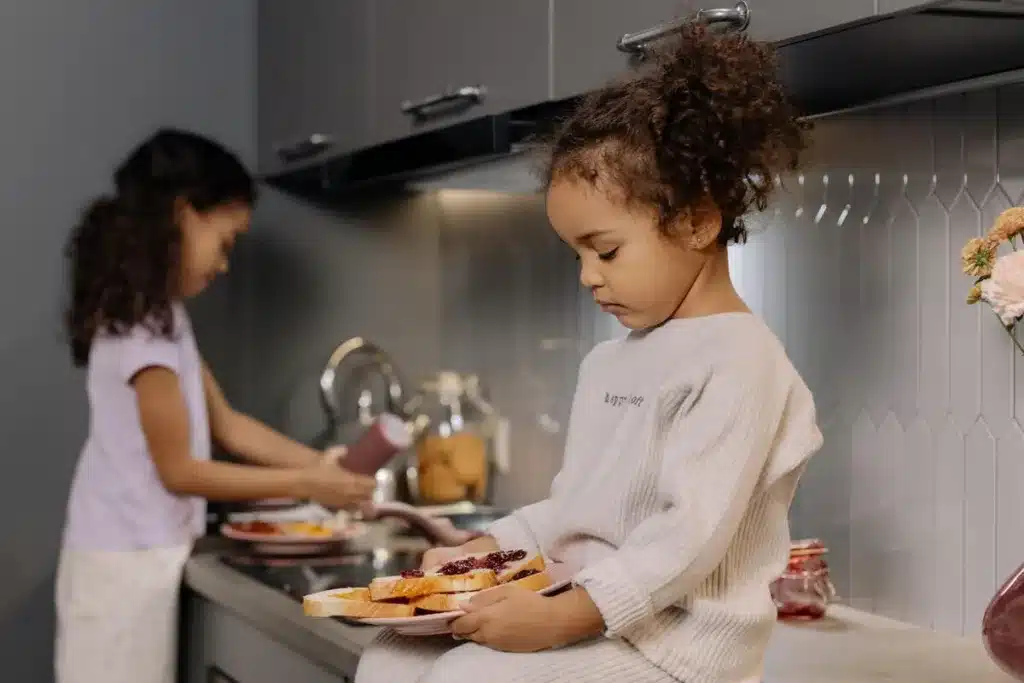 Big sister making sandwiches while little sister looks at her plate with no appetite