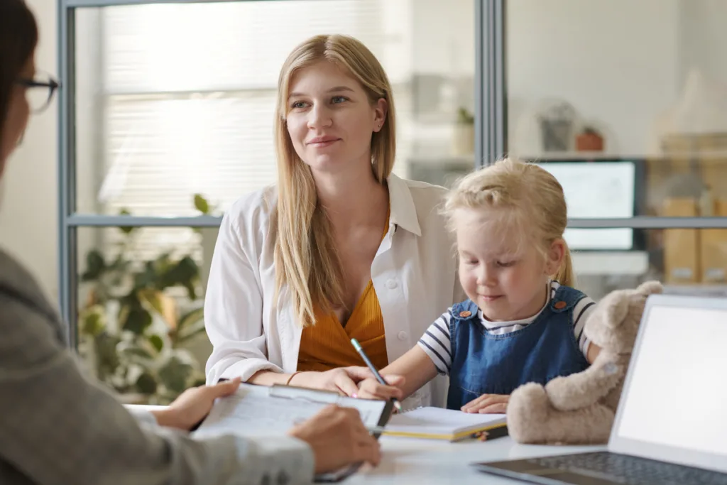 How to stop a child from biting at daycare  - A smiling mother and her daughter who is drawing are in the child care director’s office