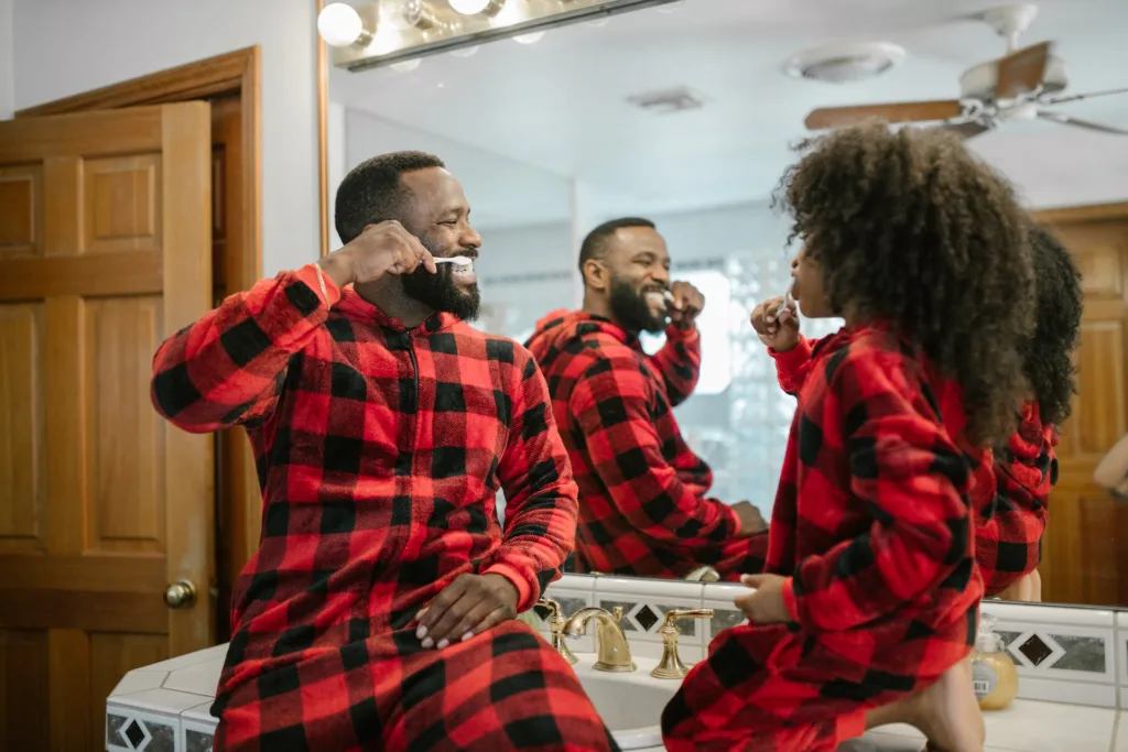 Dad and daughter in matching pajamas share a cute moment, brushing teeth together in the bathroom.