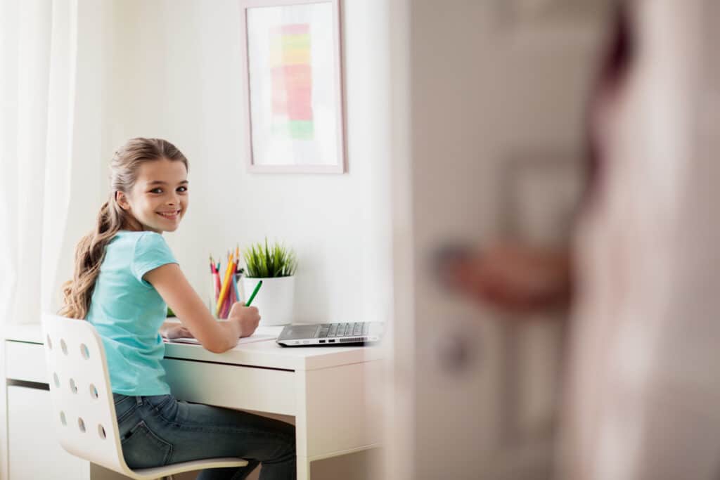 Happy schoolgirl doing homework on her tidy desk