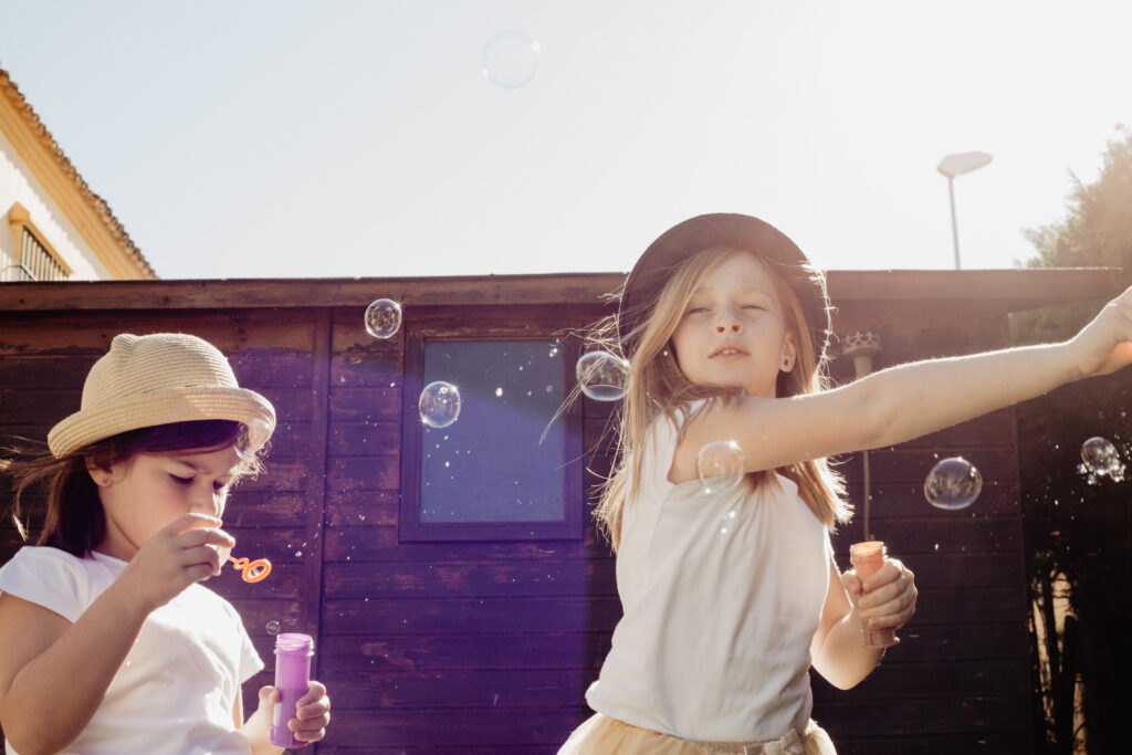 Two school-aged girls making soap bubbles in the backyard