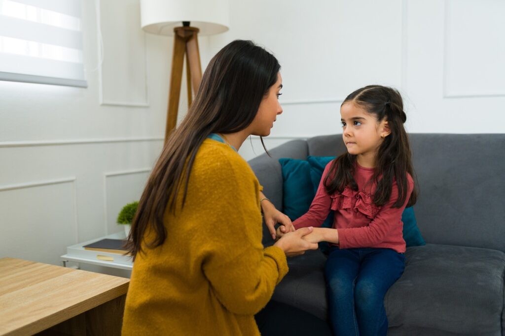 Mother lovingly holding her daughter’s hands and making eye contact while offering explanations
