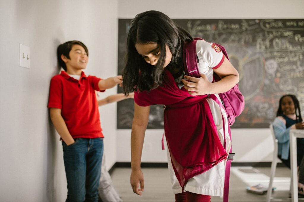 Indian schoolgirl in classroom being bullied and pointed at by other kid.