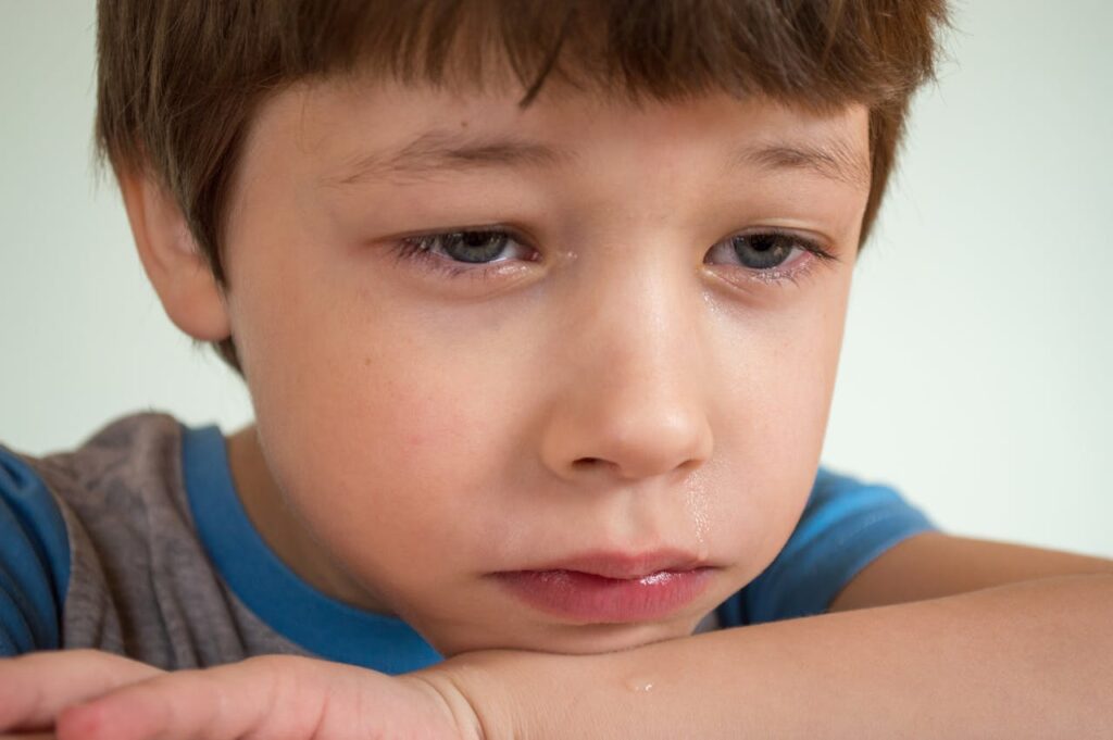 A young boy sits alone, tears streaming down his face, as he cries in distress.