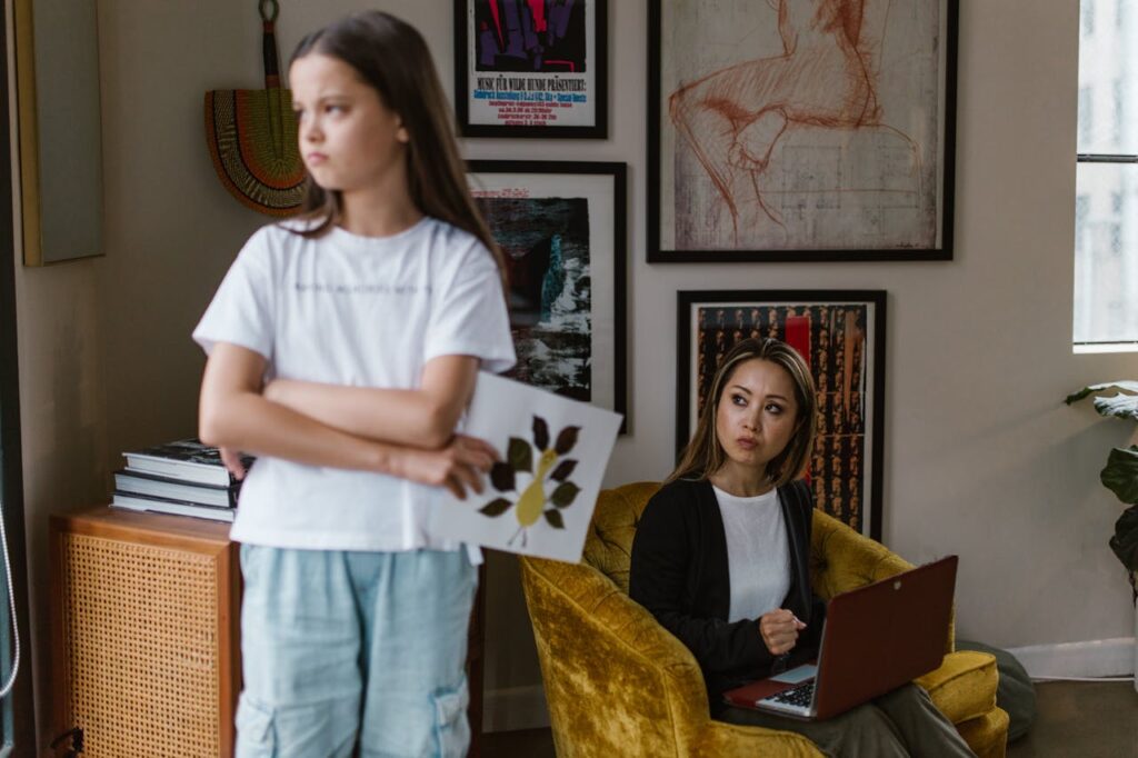 A teenage daughter stands with her back to her mother, appearing upset and distant