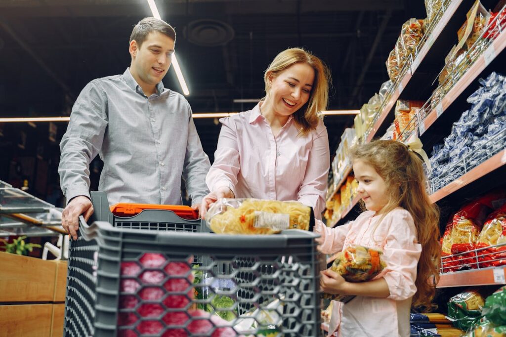 A happy family, consisting of a mom, dad, and their daughter, shopping together in a supermarket, filling their cart with groceries.





