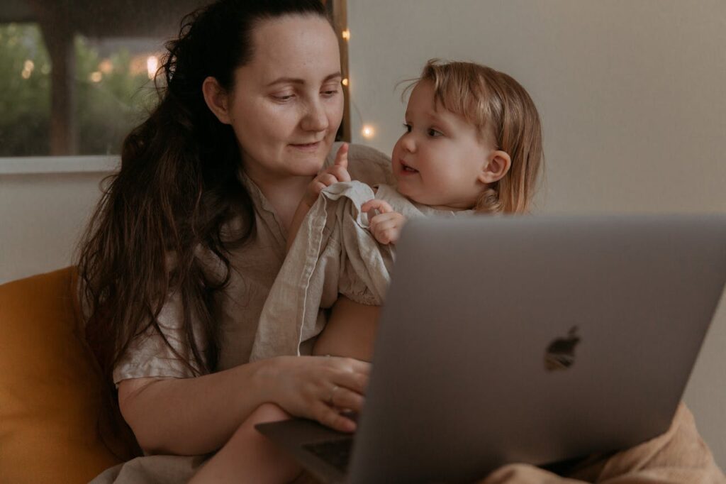 Mother working on a laptop in bed with her daughter sitting on her lap.