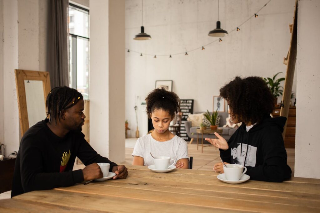 A mom and dad scolding their young daughter, who looks upset, as they stand together in a calm, but serious discussion.