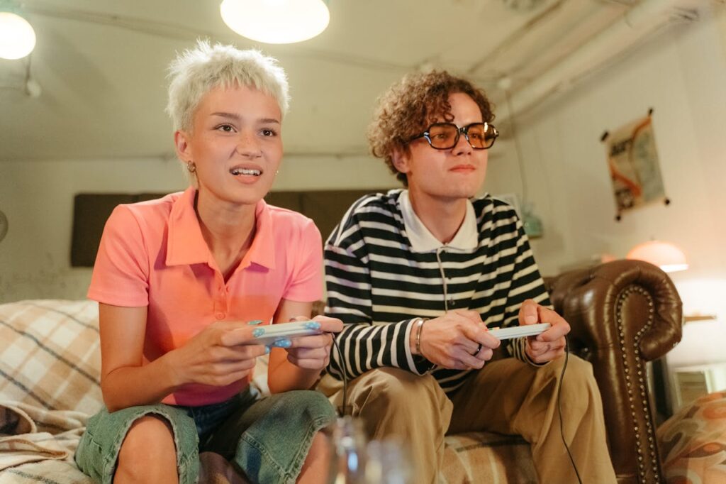 A teenage couple playing video games together on the sofa