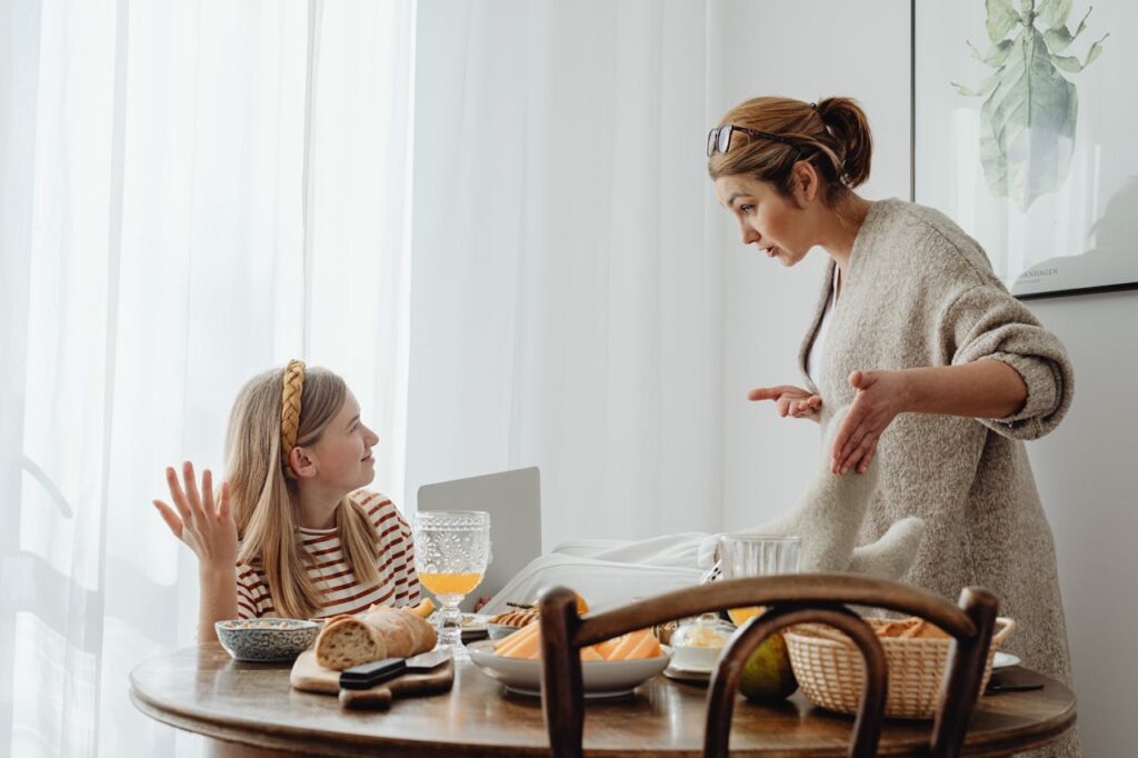 A mother argues with her teenage daughter, who has her legs on the table during a meal.