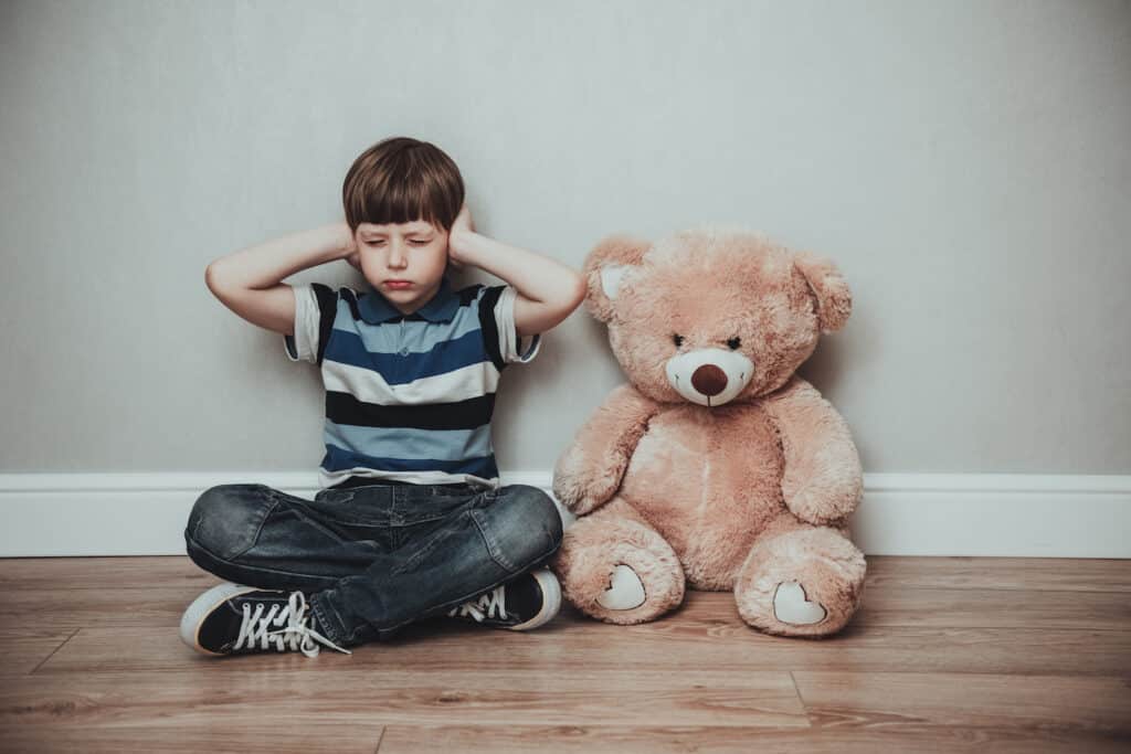 Child boy against gray background covering ears with hands eyes closed. Domestic violence and family abuse concept